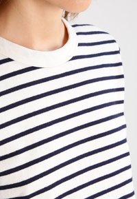 Detailní záběr osoby v bílé košili s rovnoměrně rozloženými námořnickými horizontálními pruhy a kulatým výstřihem.