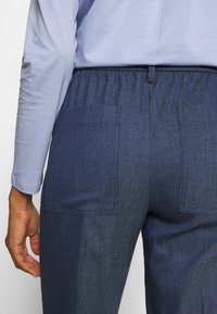 Pantalon texturé bleu foncé avec une taille élastique, doté de deux poches arrière et d'une coupe décontractée. Tissu doux visible dans le design.
