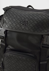 Black backpack featuring a textured pattern, smooth nylon material, zippered compartments, and a logo accent on the front.