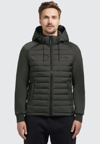 Dunkelgrüne gepadded Jacke mit Kapuze, Reißverschluss vorne und verstellbaren Kordeln. Sie verfügt über kontrastierende matte Stoffsegmente und Seitentaschen.