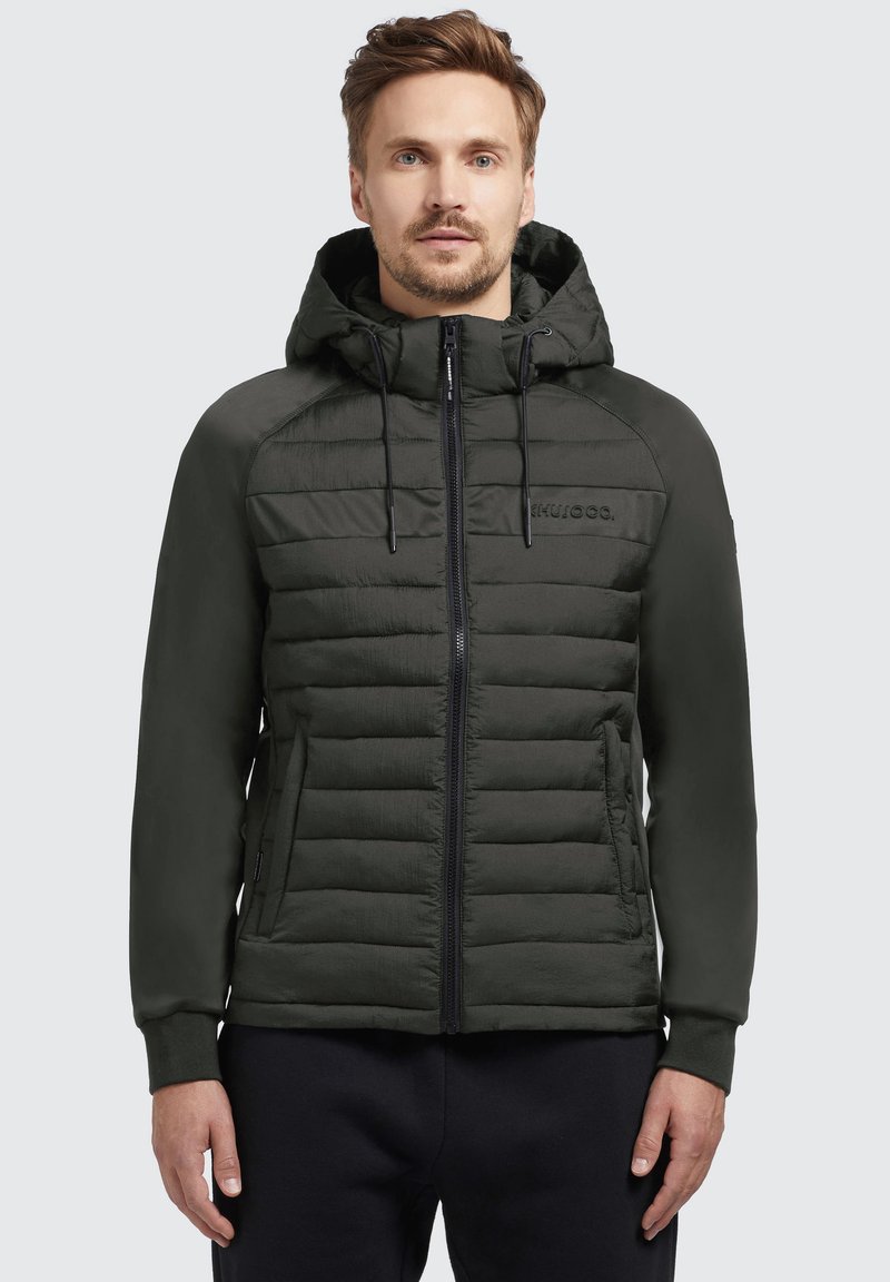 Dunkelgrüne gepadded Jacke mit Kapuze, Reißverschluss vorne und verstellbaren Kordeln. Sie verfügt über kontrastierende matte Stoffsegmente und Seitentaschen.