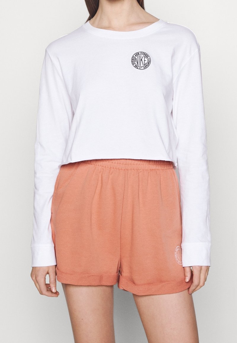 Vit långärmad croppad topp med en cirkulär logotyp, kombinerad med mjuka, persikofärgade bomullsshorts med elastisk midja och uppvikt fåll.