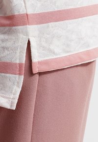 Haut blanc à rayures roses ; tissu léger et texturé ; ourlet avec accent rose ; superposé à un vêtement rose clair.