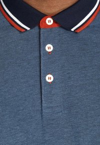 Navy blue polo shirt featuring a textured weave, red and white striped collar, and three white buttons with red stitching.