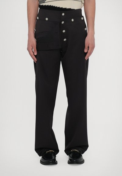 Pantalons larges noirs avec une quincaillerie métallique et une grande poche latérale, dotés d'une texture lisse et d'une coupe ajustée.