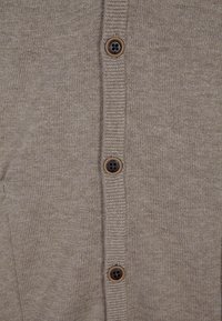 Bruine gebreide cardigan met een geribbelde textuur en zes ronde bruine knopen langs de voorkant.