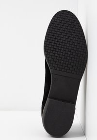 Scarpa in suede nera con suola in gomma testurizzata. La parte inferiore presenta un motivo a griglia e la marcatura della taglia "37". Il tacco è leggermente sollevato.