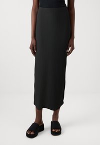 Črna rebrasta midi krila s slim fit krojem, ki ima visok pas in stranski razporek. V kombinaciji s črnimi nastavljivimi platform čevlji.