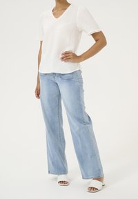 Top blanco texturizado con escote en V y mangas cortas, combinado con vaqueros anchos azul claro y sandalias blancas abiertas.