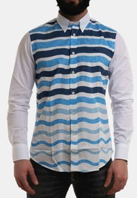Camicia botton down con onde orizzontali blu e bianche sul lato sinistro. Il lato destro è completamente bianco, con colletto classico e bottoni.