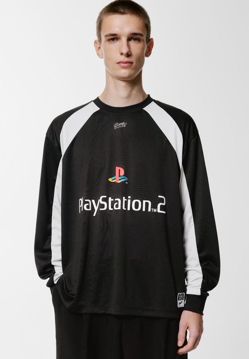 Schwarzes Langarmshirt mit weißen Raglanärmeln. Die Vorderseite zeigt das "PlayStation 2"-Logo mit mehrfarbigem Emblem. Geschmeidige Stoffstruktur.