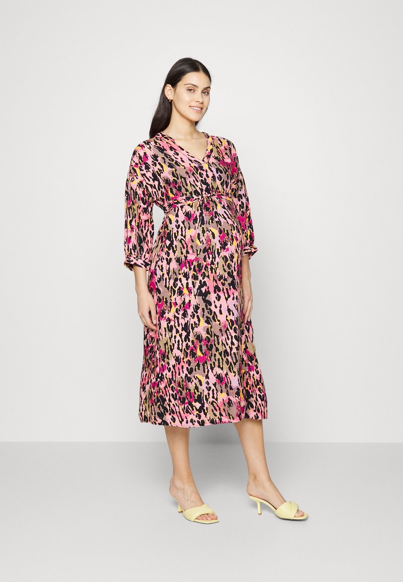 Vestido com estampa de leopardo floral em tons de rosa, preto e dourado; decote em V, mangas 3/4, cintura cintada. Combinado com sandálias amarelas de dedos abertos.