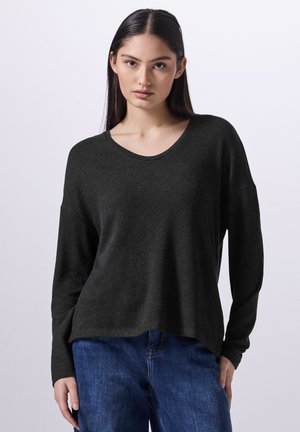 Dunkelgrauer Langarmpullover mit einem runden Ausschnitt. Weicher Stoff, lockere Passform und überschnittene Schultern, kombiniert mit blauen Denim-Jeans.