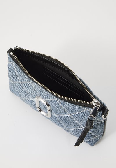 Bolsa de denim com um padrão matelassado, ferragens prateadas e fecho de zip. O interior possui um forro preto e slots para cartões. Forma retangular compacta.