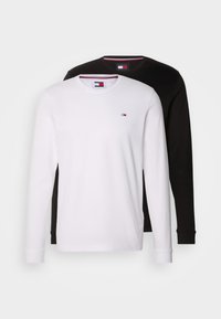 Dos camisetas de manga larga: una blanca con un logo en el pecho y una negra. Ambas tienen cuellos redondos y están hechas de una tela suave.