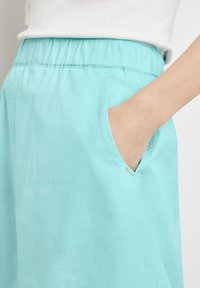 Falda azul claro con cinturilla elástica, bolsillos laterales y una textura suave. La tela parece ligera y transpirable.