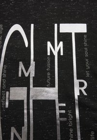 Schwarzes Stoff-T-Shirt mit metallicsilbernem Text, der abstrakte Designs und Phrasen in unterschiedlichen Schriftarten zeigt, wodurch ein strukturierter Look entsteht.