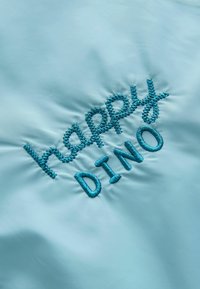 Ljusblått tyg med "happy DINO" broderat i turkos tråd. Har en mjuk textur och en lekfull typsnittdesign.