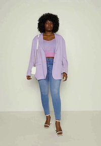 Blazer oversized lilás, top cropped rosa com padrão, jeans skinny azul claro e sandálias de salto brancas, todos num fundo neutro.