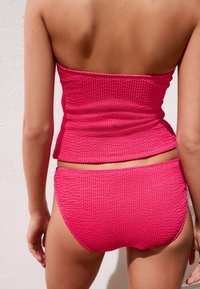 Ensemble bikini rose texturé comprenant un haut bandeau et un bas taille basse assorti, avec un motif côtelé et une finition lisse.