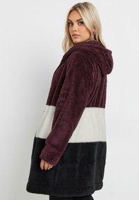 Chaqueta con capucha de felpa y bloques de color que presenta paneles de púrpura oscuro, crema y negro. Textura suave con mangas largas y un corte relajado.