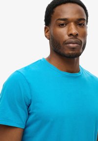 Turkis bomulds t-shirt med rund halsudskæring og korte ærmer, der har en glat tekstur og en almindelig pasform.