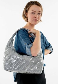 Bolso plateado acolchado hecho de material brillante, con patrones de costura en diagonal. El diseño es ancho y caído, con una correa amplia.