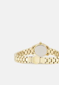Montre-bracelet en métal doré avec un cadran rond, bracelet à maillons et fermeture à cliquet. Texture lisse et design minimaliste, sans marquages visibles.