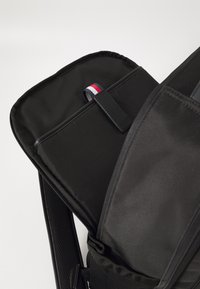 Black backpack featuring a smooth exterior, padded straps, and a top compartment with a colored fabric accent and zipper closure.