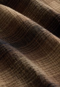 Tissu en laine marron et noir avec un motif chevron et à carreaux, présenté en plis doux et texture en gros plan.