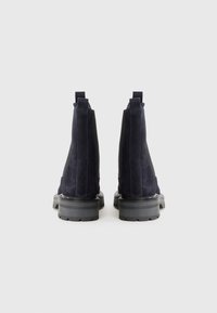 Botas de tobillo de ante negro con paneles laterales elásticos, tiradores y suelas de goma texturizada. Diseñadas con una silueta elegante y acentos mínimos.