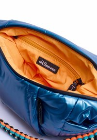 Sac à main en nylon bleu moelleux avec doublure orange, poche zippée, étiquette de logo et une bandoulière tressée multicolore. Présente une surface brillante et texturée.