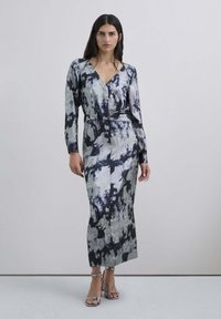 Abito lungo a maniche lunghe, stile incrociato, con un motivo astratto argentato e blu, realizzato in un tessuto liscio e lucido; presenta una silhouette aderente e una gonna lunghezza pavimento.