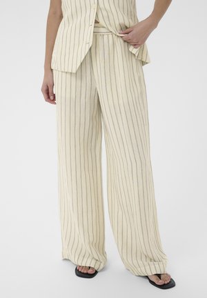 Beżowe spodnie o szerokich nogawkach w cienkie pionowe szare paski, połączone z dopasowanym bezrękawnikiem i czarnymi sandałami na kwadratowym nosku.