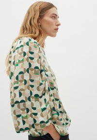 Bluză cu mânecă scurtă, cu un fundal crem și modele geometrice în verde, maroniu și bej, realizată dintr-un material ușor.