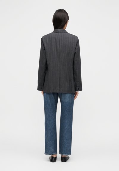 Blazer gris à rayures fines avec une coupe ajustée, tissu léger, col cranté, manches longues et deux boutons aux poignets, porté avec un jean bleu à jambes larges.