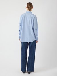 Light blue striped shirt with a loose fit, features rolled-up sleeves and a curved hem, paired with wide-leg dark denim pants.