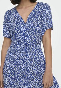 Niebieska sukienka w kwiaty z dekoltem w serek, krótkimi rękawami, wiązaniem w talii oraz lekkim materiałem z białymi wzorami kwiatowymi.