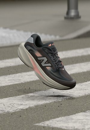 Sort og grå New Balance løbesko med pink accenter svævende over et fodgængerfelt på en byens gade.