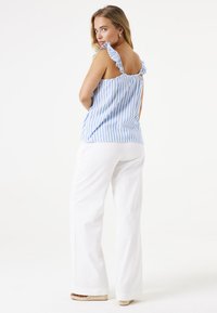 Blauw en wit gestreepte top met rimpelbandjes, gecombineerd met witte wijde broek en platform espadrilles. Glad stofoppervlak.
