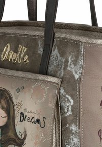 Beige synthetische Tragetasche mit dunkelbraunen Trägern; verfügt über eine Fronttasche mit einer Mädchenillustration und dem Text "Die Welt der Träume."