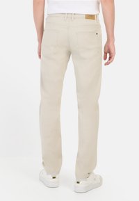Beige gerade geschnittene Hose mit glatter Oberfläche, ausgestattet mit zwei Gesäßtaschen und einem markierten braunen Lederpatch am Bund.