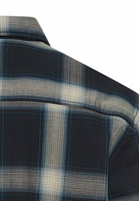 Czarna i niebieska koszula w kratę, wykonana z materiału o fakturze, z kołnierzykiem na guziki i detalami na karczku z tyłu.