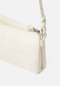 Witte gestructureerde leren clutchbag met een decoratief reliëfpatroon, voorzien van een ritssluiting en een verstelbare schouderband.