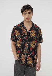 Koszula z krótkim rękawem na czarnym tle, z kolorowym wzorem kwiatowym i tygrysim. Wykonana z lekkiego materiału, w luźnym fasonie.