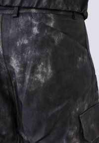 Schwarze strukturierte Hose mit einem marmorierten Muster. Verfügt über schräge Taschen und einen stabilen Bund, gefertigt aus einem lederähnlichen Material.