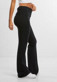 Black flared pants made of soft knit fabric featuring a ribbed waist and a wide leg design, paired with white sneakers.