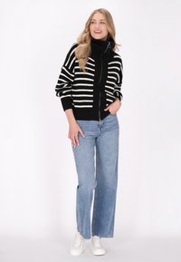 Zwart-wit gestreepte zip-up jas met hoge kraag, gecombineerd met lichtblauwe wijde jeans en witte sneakers.