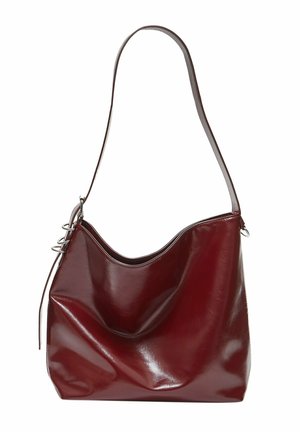 Sac à épaule en cuir rouge foncé avec une bandoulière unique et des détails en boucle argentée sur un côté.