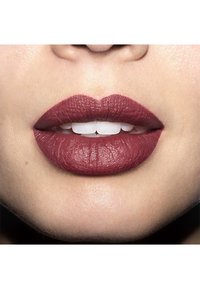 Matte, deep berry lipstick applied to full lips, showcasing fine texture and defined contours, against a soft, neutral skin background.